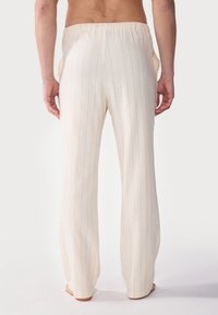 Avslappede kremfargede loungebukser med vertikale pinstriper, elastisk liv, og sidelommer. Myk tekstur, rett ben-design.