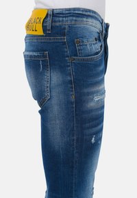 Denim jeans in een middelblauwe wassing, met versleten details, twee achterzakken en een gele label met "BLACK BULL" op de tailleband.