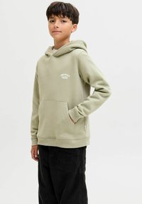 Felpa verde chiaro con tasca a marsupio e polsini a coste. Presenta un logo "ORIGINALS" bianco sul petto. Abbinata a pantaloni in velluto a coste neri.