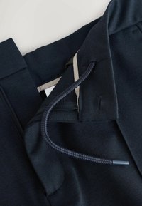 Granatowy materiał z elastycznym paskiem ze sznurkiem i zamkiem błyskawicznym, z kontrastującym jasnym akcentem. Gładka tekstura i czysty design.
