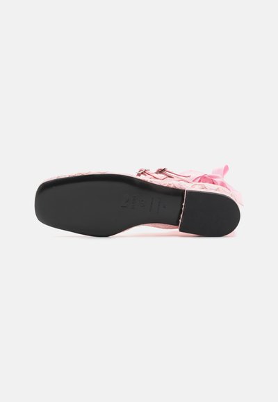 Zapato texturizado rosa con una suela de goma negra, que presenta un acento de lazo y hardware metálico. La parte superior está decorada con un patrón tejido.