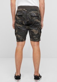 Karinės kamufliažo stiliaus kelnaitės iš medvilnės. Turi šonines kišenes, atlenkiamus kraštus ir elastingą juosmenį. Spalvos: tamsiai žalia ir ruda.