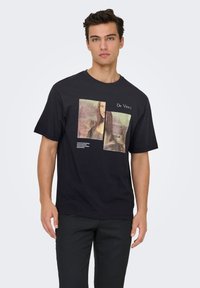 Sort bomuld T-shirt med et grafisk tryk af Mona Lisa, med teksten "Da Vinci" i hvid under billedet. Korte ærmer, rund hals.
