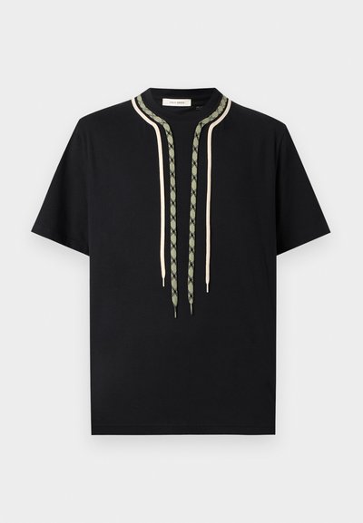 Μαύρο κοντομάνικο μπλουζάκι με δύο μακριές διακοσμητικές κορδόνια, ένα μπεζ και ένα πράσινο με σχέδιο, να κρέμονται από το γιακά.