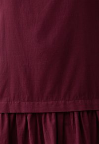 Abito bordeaux con una texture liscia e leggera, caratterizzato da un orlo arricciato con volant e da un design semplice e senza fronzoli.