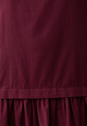 Bordowa sukienka o gładkiej, lekkiej teksturze, z marszczonym, falbanowym dołem oraz prostym, nieozdobionym wzornictwem.