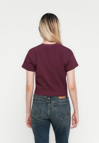 Gecropte, kortearmige t-shirt van donker bordeaux katoen. G gedragen met hoge taille blauwe denim jeans met een leren label.