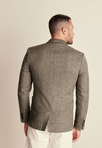 Grau gemusterter Blazer im Fischgrätmuster mit taillierter Passform, strukturierten Schultern und belüftetem Rücken, mit schwarzen Knöpfen an den Ärmeln.
