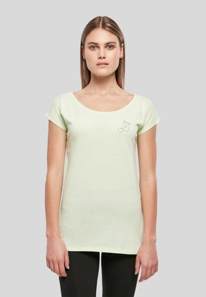 Jeune femme aux cheveux châtain clair et raides portant un t-shirt vert pâle à manches courtes avec un petit motif de cerise sur la poitrine.