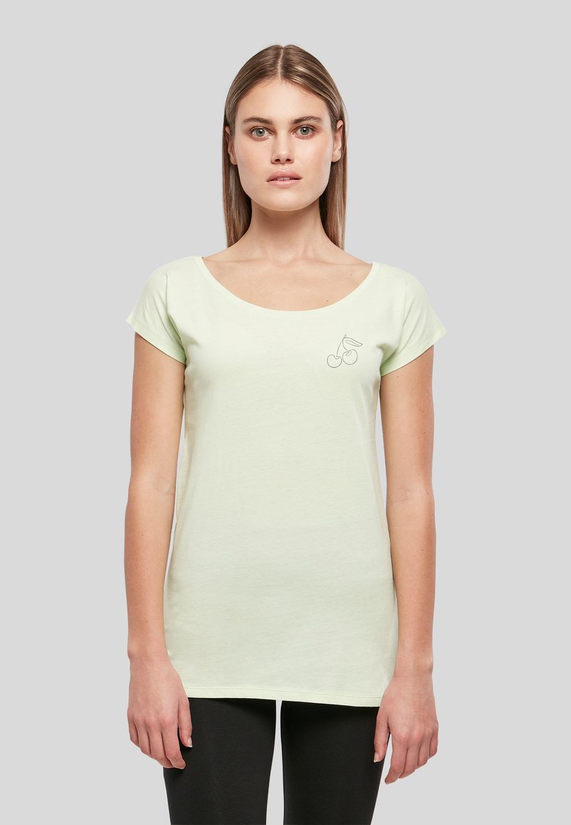 Jeune femme aux cheveux châtain clair et raides portant un t-shirt vert pâle à manches courtes avec un petit motif de cerise sur la poitrine.