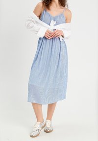 Robe midi rayée bleu et blanc avec fines bretelles, taille cintrée et silhouette fluide, associée à des baskets argentées.