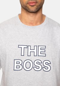 Graues Baumwoll-T-Shirt mit Rundhalsausschnitt und auffälligem, navyblauen Text, der "THE BOSS" quer über die Vorderseite gedruckt ist.