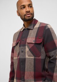 Karierte Hemd in dunklen Rot-, Braun- und Schwarztönen. Verfügt über zwei Brusttaschen, Knopfverschluss und einen Kragen. Hergestellt aus einem strukturierten Stoff.