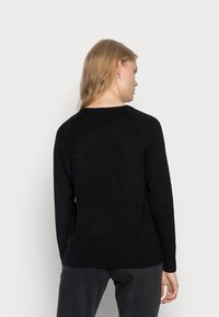Black knitted sweater with long sleeves, a round neckline, and ribbed cuffs and hem. Smooth texture, fitted design, worn with gray jeans.