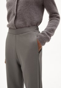 Grijze hooggetailleerde broek van gladde stof, met zijzakken en een gestructureerde tailleband met subtiele plooien, gecombineerd met een gebreid sweater.