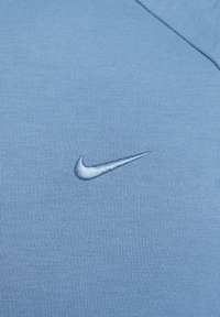 Tissu bleu clair avec un logo Nike swoosh cousu près du col d'un vêtement.
