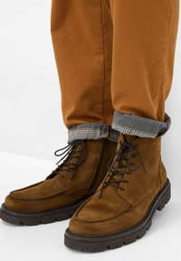 Braune Wildleder Schnürstiefel mit einer stabilen Gummisohle. Der Schaft ist grau mit einem kleinen Punktmuster. Einfaches Design mit glatter Textur.