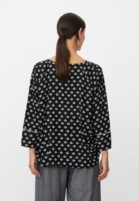 Zwart topje met een geometrisch patroon met lichtblauwe en gele accenten, driekwart mouwen en een losse pasvorm.