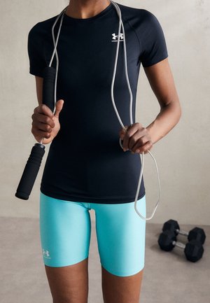 Person i sort Under Armour-shirt og turkis shorts holder et sjippetov med håndvægte på gulvet bag dem.
