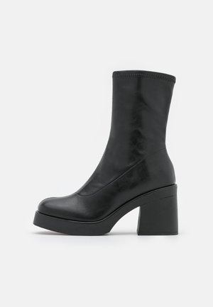 Bottine en cuir noir avec talon bloc épais et bout arrondi, texture lisse et détail de bord supérieur cousu.