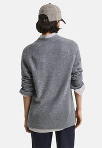 Grauer Strickpullover mit umgeschlagenen Ärmeln, geripptem Saum und einem geschichteten Look über einem gestreiften Hemd. Hat eine weiche Textur und ein lässiges Design.