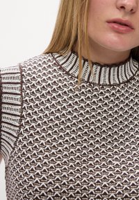 Brun og hvid mønstret strikket sweater med høj hals, der har et tekstureret design og kontrasterende ribbede detaljer på skuldrene.