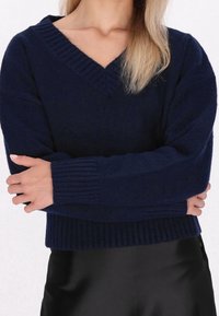 Pull col en V bleu marine en maille douce, avec poignets et ourlet côtelés, coupe décontractée et détail de couture texturée.