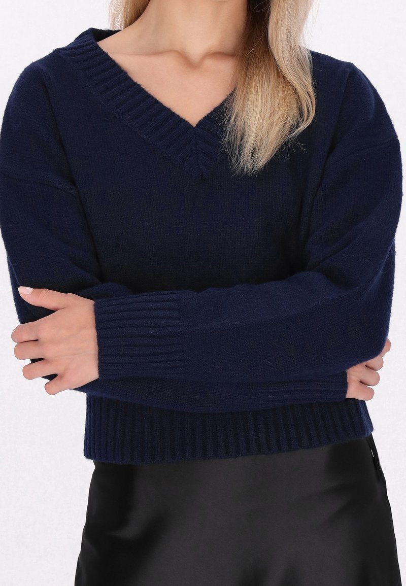 Pull col en V bleu marine en maille douce, avec poignets et ourlet côtelés, coupe décontractée et détail de couture texturée.