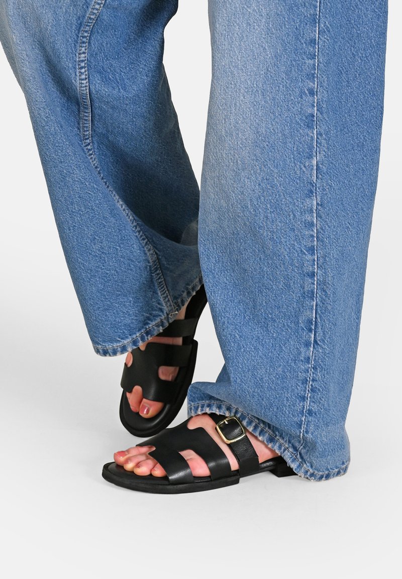Zwarte leren sandalen met brede bandjes en een gespsluiting, gedragen met lichtblauwe denim, wat zorgt voor een ontspannen pasvorm en rafelige zomen.