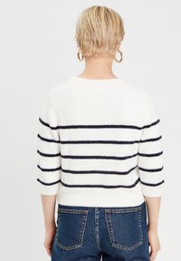 Maglione bianco con righe orizzontali blu navy, texture morbida e maniche a tre quarti. Abbinato a jeans blu a vita alta.