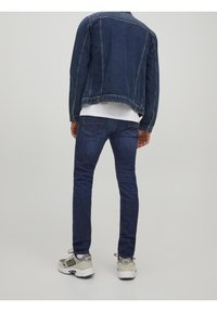 Jeansjacka i mörkblått med framlommer, bärs över en vit skjorta, kombinerad med mörkblå skinny jeans och ljusgrå sneakers.