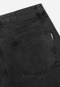 Black denim jeans featuring a textured finish, five-pocket design, and branded leather patch on the waistband.