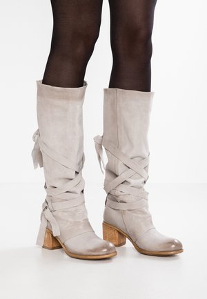 Bottes en daim grises jusqu'au genou avec un talon en bois empilé. Présente des sangles croisées et une texture lisse, mettant en avant un design minimaliste.