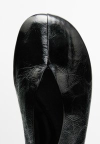 Ballerines noires en matériau synthétique texturé, avec un bout arrondi et un design découpé à l'avant. Fini lisse et brillant.