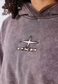Sudadera con capucha gris de tejido texturizado, con un logotipo bordado en marrón oscuro "PXP" y un emblema de estrella en el pecho.