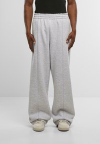 Gaiši pelēkas sporta bikses, kas izgatavotas no mīksta auduma ar elastīgu jostasvietu, piedāvā brīvu piegriezumu un sānu šuvju detaļas. Pāris ar gaišiem sporta apaviem.