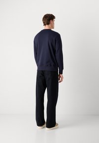 Navyblauwe sweatshirt met geribbelde manchetten en zoom, gecombineerd met zwarte wijde broek en beige sneakers, gezien vanuit de rug.
