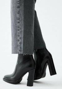 Stivaletti alla caviglia in pelle nera con tacco robusto, punta arrotondata e cerniera laterale. Abbinati a jeans grigi corti leggermente consumati.