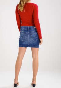 Červený dlouhý rukáv top doplněný modrou denimovou mini sukní. Sukně má zadní kapsy a úzký střih, s hladkou strukturou a lemováním.