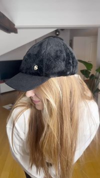 Svart lue i kunstpels med svart skygge, med et lite hvitt brodert nummer 8 foran. Myk tekstur og strukturert form.