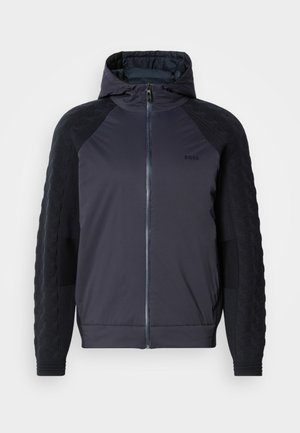 Kurtka z kapturem w ciemnym granacie z zamkiem z przodu, teksturowane czarne rękawy z geometrycznym wzorem oraz ściągacze w pasie.