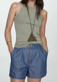 Top sin mangas acanalado de color verde oliva combinado con pantalones cortos de mezclilla azules. Los pantalones cortos tienen un corte relajado, bolsillos y un cierre de botón en la parte delantera.