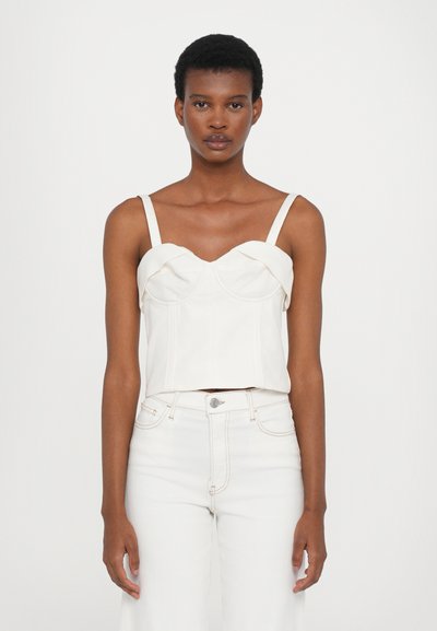 Haut court blanc avec un bustier structuré, des fines bretelles et de subtiles plis. Associé à un jean blanc taille haute avec des coutures visibles.