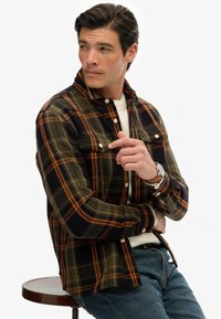 Geklede shirt in donkergroen, marineblauw en oranje; knoopsluiting aan de voorkant; twee borstzakken; klassieke kraag; gestructureerde stof; gedragen over een witte trui.
