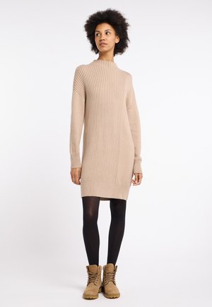 Robe en tricot côtelé beige avec un col montant et des manches longues, associée à des collants noirs et des bottes à lacets beige.