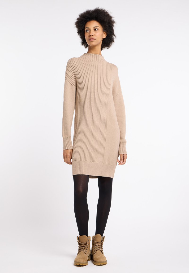 Beige geripptes Strickkleid mit hohem Kragen und langen Ärmeln, kombiniert mit schwarzen Strumpfhosen und hellbraunen Schnürstiefeln.