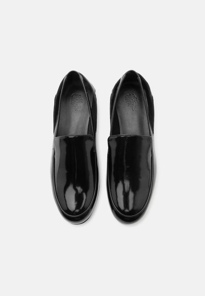 Ζευγάρι μαύρα, γυαλιστερά δερμάτινα loafers χωρίς κορδόνια με στρογγυλεμένες μύτες, απόψη πάνω σε απλό ανοιχτό φόντο.