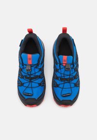 Zapatillas deportivas azules con acentos negros, cordones elásticos, lengüetas rojas, parte superior de malla texturizada y suelas robustas para una mejor adherencia.