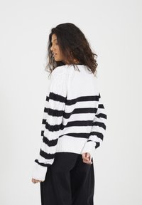 Czarny i biały sweter z dzianiny w paski, z teksturowanym wzorem na ramionach, ściągaczem u dołu i długimi rękawami. Luźny fason z relaksującą sylwetką.