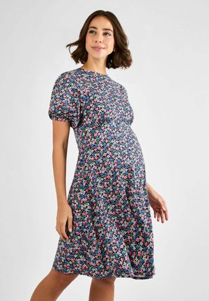 Robe de maternité florale avec des manches courtes bouffantes, un col rond, une silhouette fluide, et un fond bleu foncé avec des motifs roses et verts.